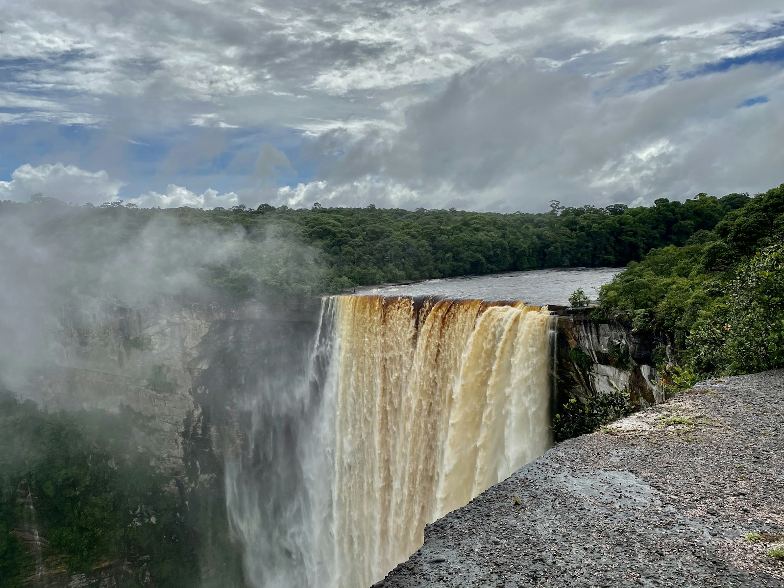 Kaieteur Falls in Guyana, brown water dropping over a cliff into rainforest under a cloudy sky