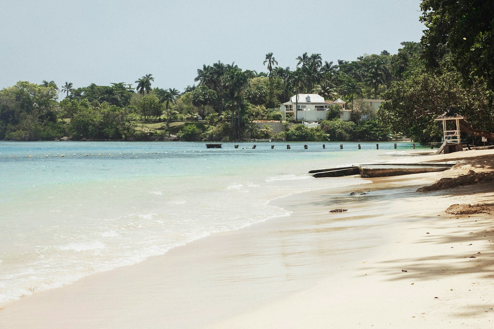 White sand beach and calm turquoise water at Ocho Rios, Jamaica, with palms and a seaside house beyond